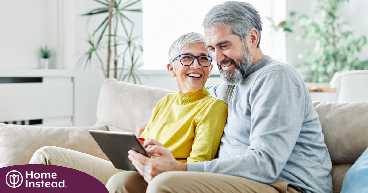 A senior couple smiles while looking at a laptop, showing how online resources can help family caregivers.