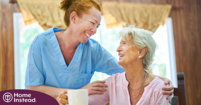 A caregiver and client smile while the caregiver hugs and helps the client, representing professional caregiving.