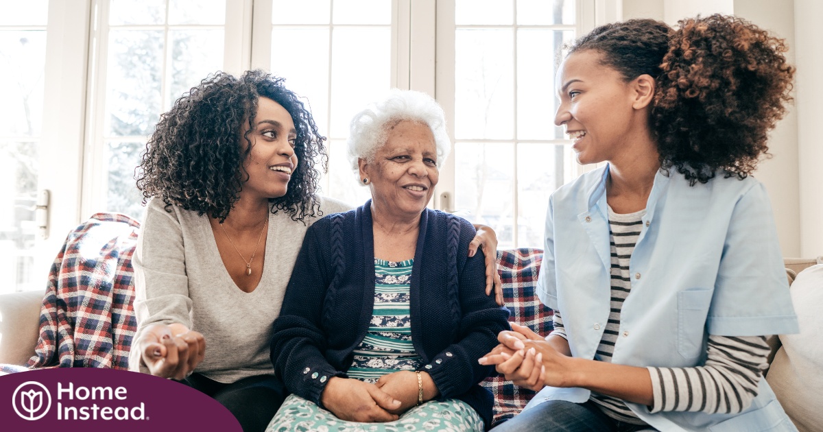 A caregiver talks with a client and her daughter, representing the type of communication that is vital when taking on a person-centered care approach.